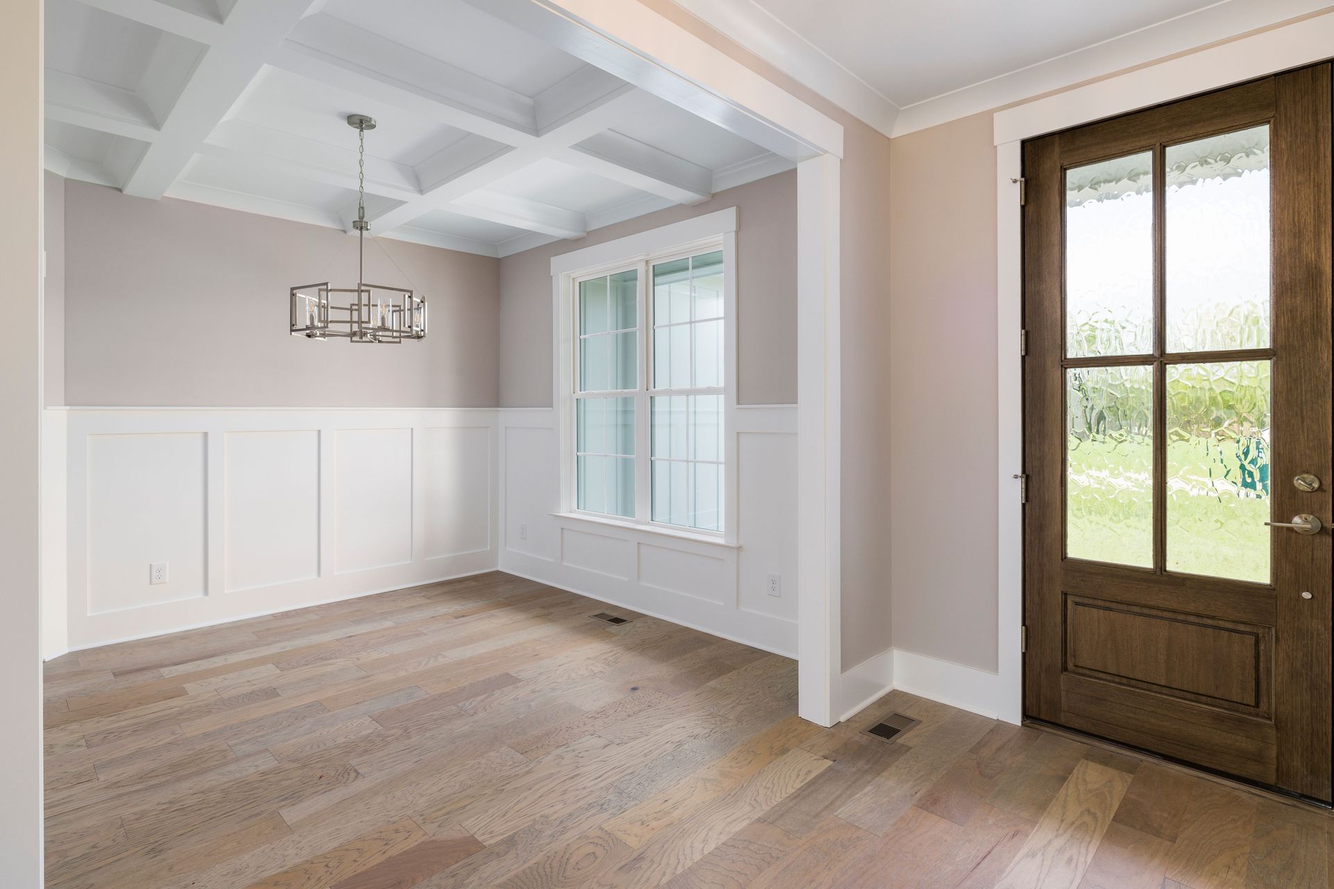A modern interior featuring a wooden door, chandelier, and parquet flooring with large windows.