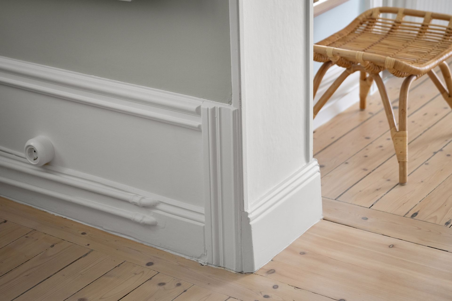 Stylish minimalist interior featuring a wooden floor, wicker chair, and elegant molding.