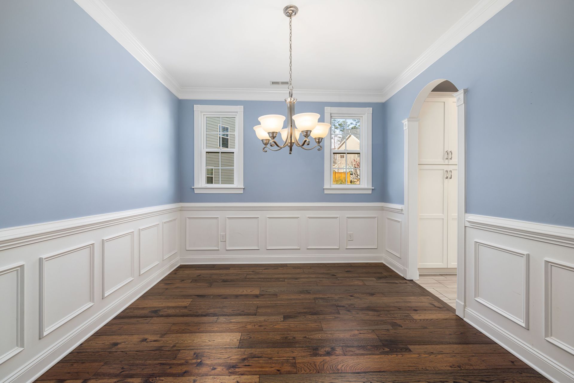 Spacious empty room with blue walls, wooden floor, and elegant chandelier lighting.