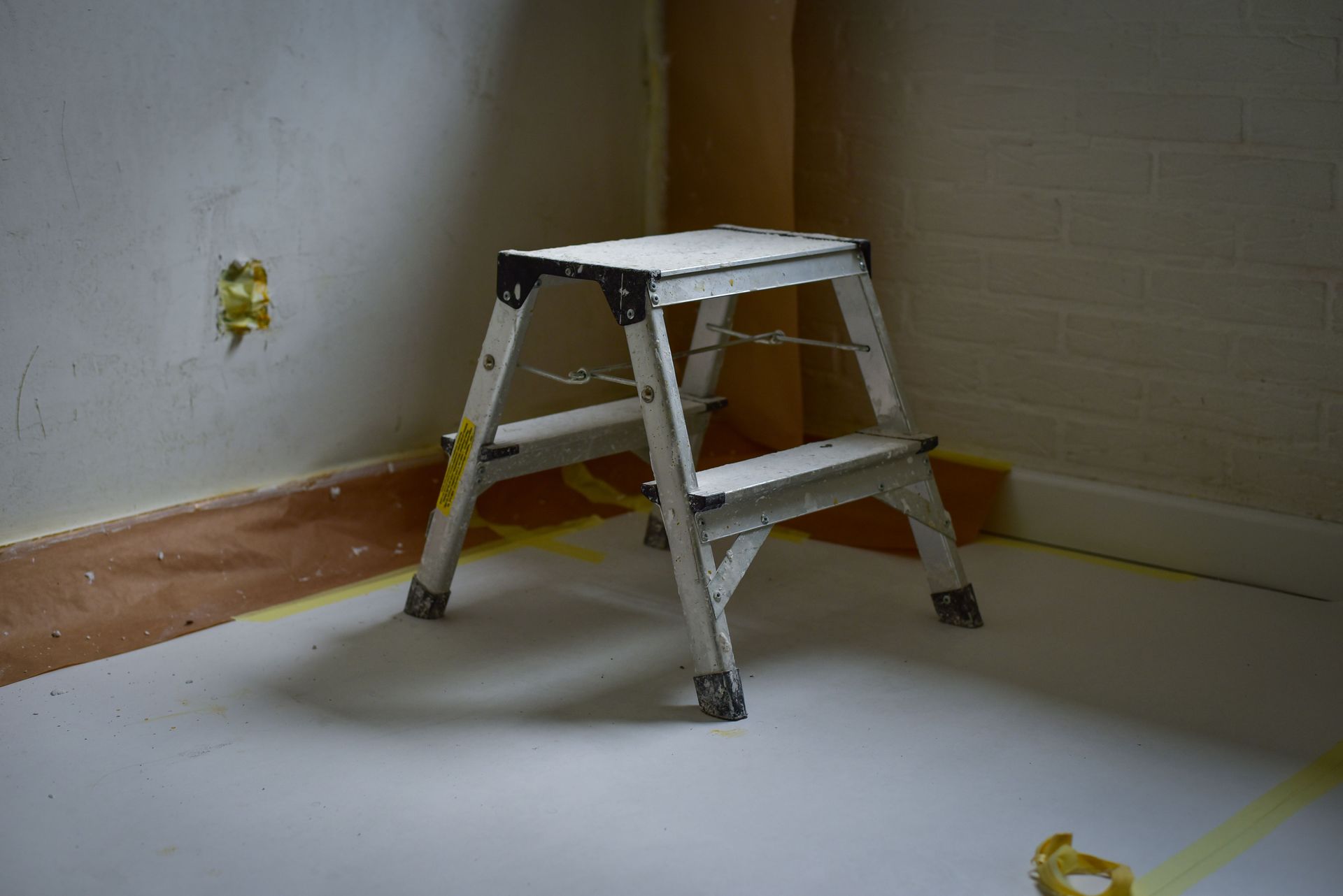 A sturdy metal ladder placed on a taped-off floor in a room under renovation.